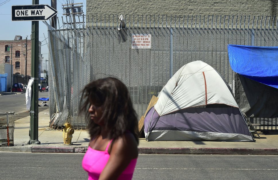 A woman walks past a sign posting the ordinance&nbsp;that led to the explosion of tents housing the homeless on Los Angeles s