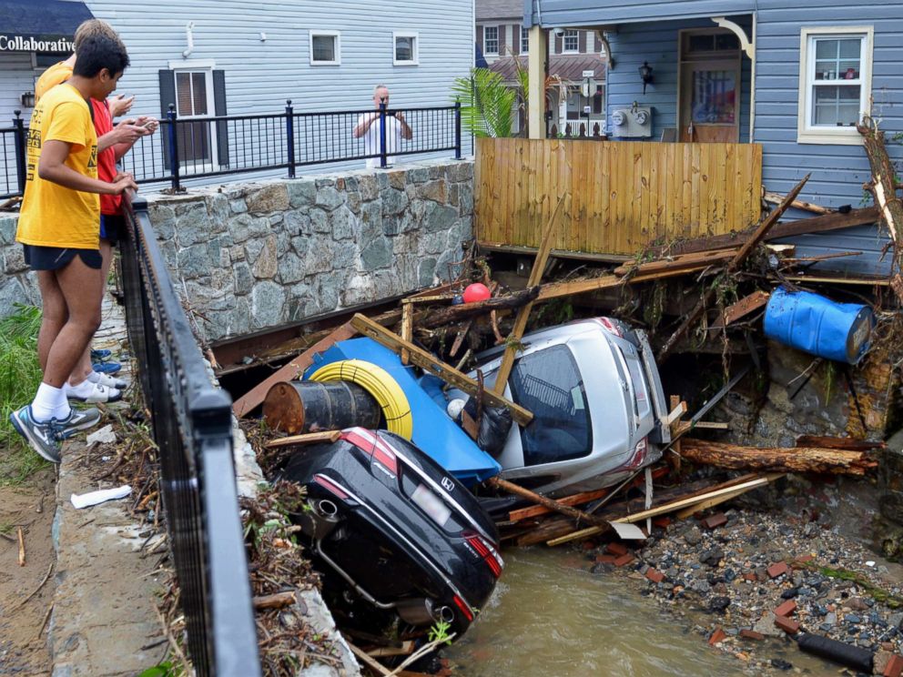 PHOTO: Residents gather by a bridge to look at cars left crumpled in one of the tributaries of the Patapsco River that burst its banks as it channeled through historic Main Street in Ellicott City, Md., May 28, 2018.