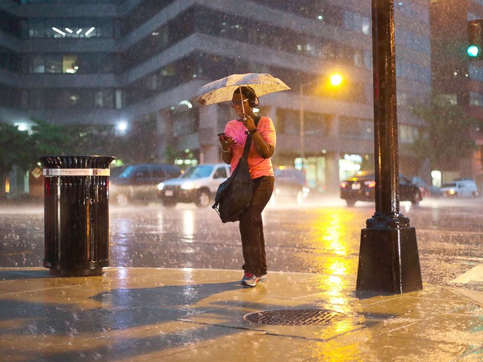 PHOTO: A woman checks her cell phone as she walks in the heavy rain showers in downtown Washington, May 14, 2018.