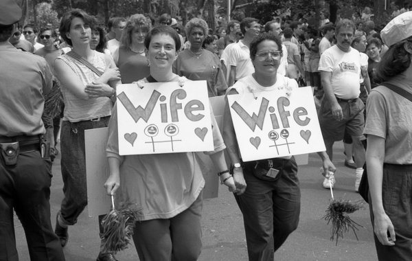 Two women wearing 'Wife' signs around their necks, smile for the camera, at the 1989 gay Pride parade in Greenwich Village, M