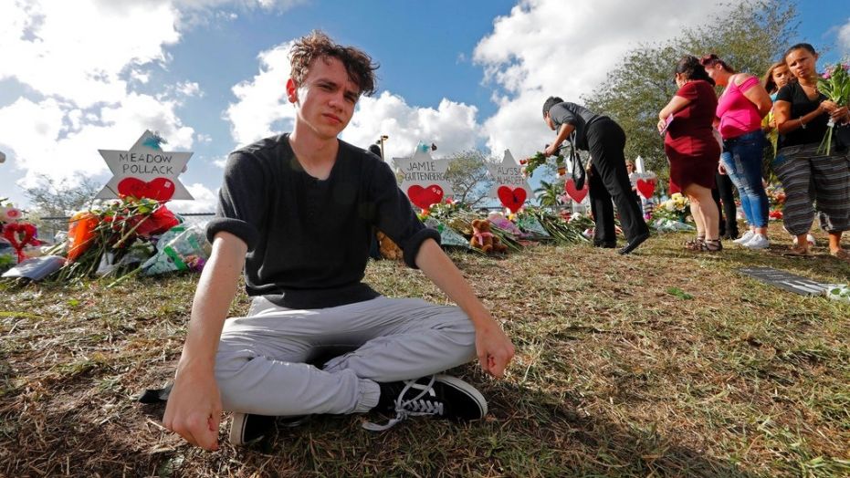 FILE- In this Feb. 19, 2018, file photo, Chris Grady, a student at Marjory Stoneman Douglas High School, sits at a memorial  in Parkland, Fla., for those slain in the Feb. 14 school shooting. Grady who had planned to join the U.S. Army before the shooting, has withdrawn his enlistment and will now work for the March for Our Lives movement. (AP Photo/Gerald Herbert, File)