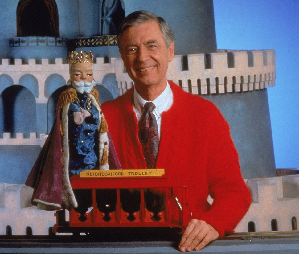 A portrait of Fred Rogers posing with a toy trolley on the set of his television show "Mister Rogers' Neighborhood" in the 19