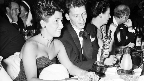 FILE - In this March 11, 1946 file photo, at a crowded table at Ciro's, Frank Sinatra steals a glance at his Oscar which he won for his performance in the film "The House I Live In," as his wife Nancy looks on at left. Nancy Sinatra Sr., the childhood sweetheart of Frank Sinatra who became the first of his four wives and the mother of his three children, has died. She was 101. Her daughter, Nancy Sinatra Jr., tweeted that her mother died Friday, July 13, 2018.  (AP Photo/File)