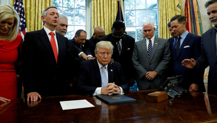 Faith leaders place their hands on the shoulders of President Donald Trump as he takes part in a prayer for those affected by