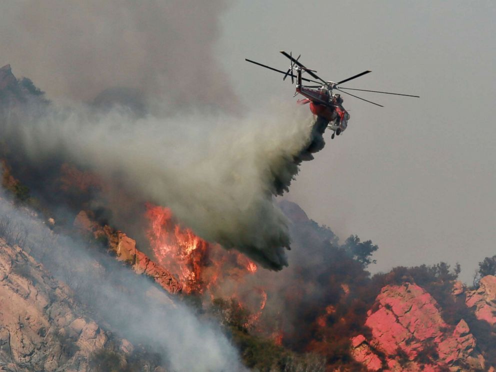 PHOTO: A helicopter drops flame retardant on a wildfire, Nov. 10, 2018, in Malibu, Calif. The Woolsey fire has burned over 70,000 acres and has reached the Pacific Coast as it continues grow.
