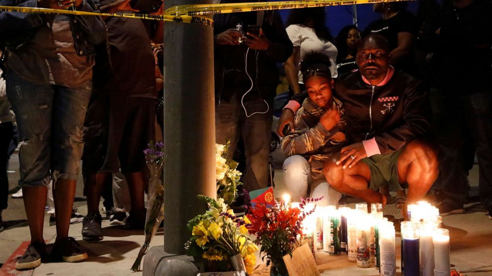 Haitian-French actor Jimmy Jean-Louis and his daughter Jasmin, 16, gather around candles set up across from the clothing store of rapper Nipsey Hussle in Los Angeles, March 31, 2019. Hussle, the skilled and respected West Coast rapper who had a decade-long success with mixtapes but hit new heights with his Grammy-nominated major-label debut album in 2018, was killed in a shooting.