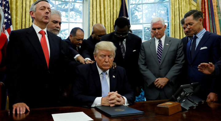 Faith leaders place their hands on the shoulders of President Donald Trump in the Oval Office as he takes part in a prayer on