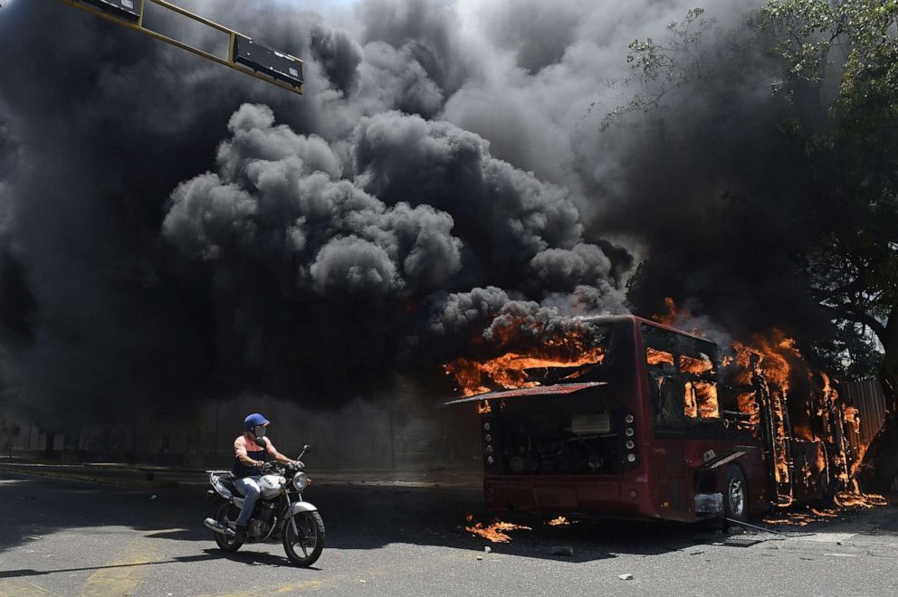 PHOTO: An opposition demonstrator passes by a government bus set on fire during clashes with soldiers loyal to Venezuelan President Nicolas Maduro after troops joined opposition leader Juan Guaido in his campaign to oust Maduro in Caracas, April 30, 2019.