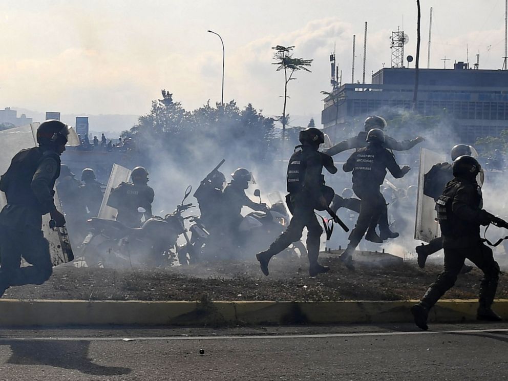 PHOTO: Members of the Bolivarian National Guard loyal to Venezuelan President Nicolas Maduro run under a cloud of tear gas after being repelled with rifle fire by guards supporting Venezuelan opposition leader Juan Guaido in Caracas, April 30, 2019. 