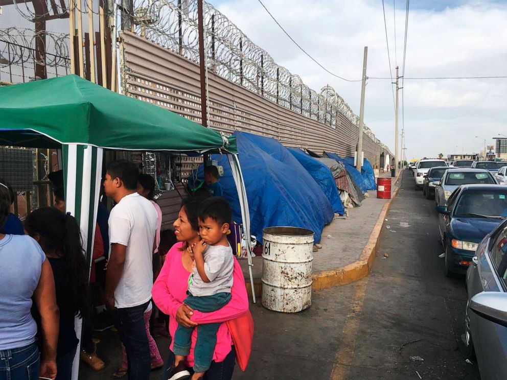 PHOTO: Migrants walk between tents, left, and cars waiting to cross the border between Mexico, and Arizona, May 5, 2019. The tent slots are for families about to be called, allowing them to be ready on a moments notice. 