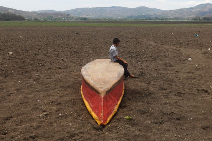 A boy sits on an abandoned boat on what is left of drought-parched Lake Atescatempa in Guatemala.
