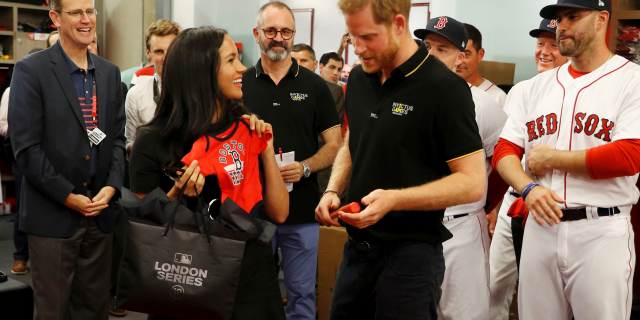 Duchess Meghan (L) and Prince Harry (R) are gifted a onesie from the Boston Red Sox. 