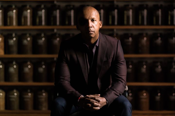 Bryan Stevenson sits in front of a wall of jars filled with soil collected from lynching sites across the country. The jars a