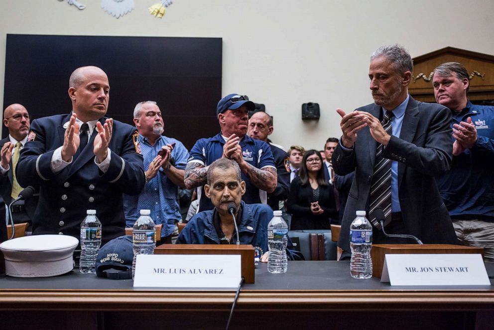 PHOTO: Michael OConnelll, left, John Feal, center, and Jon Stewart, right, applaud Luis Alvarez during a House Judiciary Committee hearing on reauthorization of the September 11th Victim Compensation Fund.