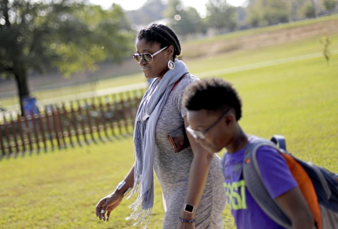 In this Oct. 11, 2017 file photo, Corrie Davis, left, picks up her son Turner from Big Shanty Elementary School in Kennesaw, Ga. The previous month, the school invited fifth-graders to dress up as characters from the Civil War. Davis says a white student dressed as a plantation owner approached her son and said 