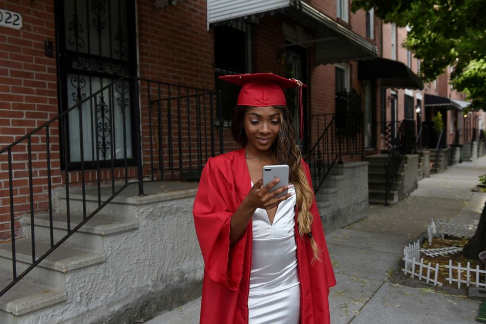 PHOTO: Francina Townes, 18, dressed for her high school graduation from Woodlawn High School, looks at her mobile phone while standing in front of her house in Baltimore, Maryland, U.S., June 8, 2019.