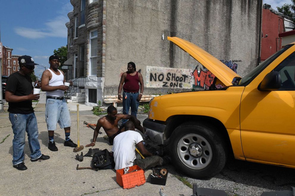 PHOTO: Isiah Dixon, center, works on his truck while surrounded by other men in Baltimore, Maryland, May 26, 2019.