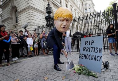 PHOTO: A man in a giant Boris Johnson head digs a grave at the foot of a pretend tombstone outside Downing Street in London, Aug. 28, 2019.