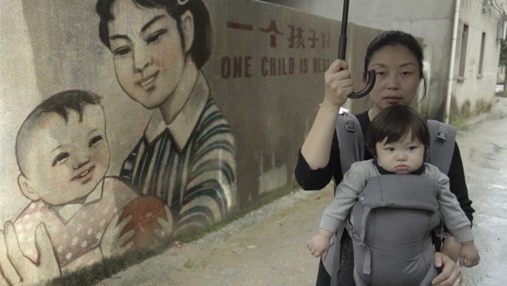 "One Child Nation" co-director Nanfu Wang and her son, next a propaganda mural promoting China's one-child policy.