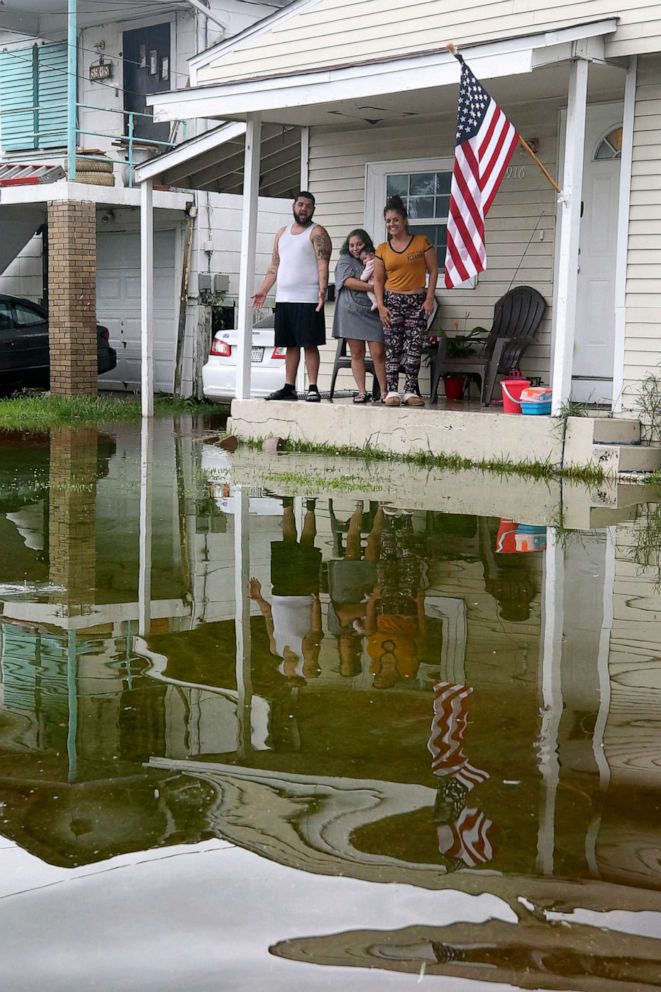 PHOTO: Mark Bazan, left, Lola Sierra, center, holding her baby, Melani, and Amanda Huschle look out over their flooded yard in Galveston, Texas, Sept. 18, 2019, after heavy rain from Tropical Depression Imelda caused street flooding.