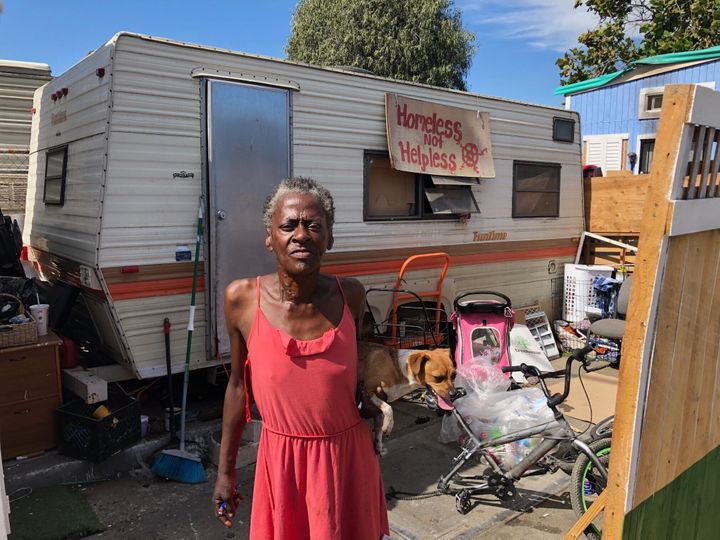 Claudette Smith stands in front of her mobile home in an Oakland homeless encampment, with a sign that reads: "Homeless not h