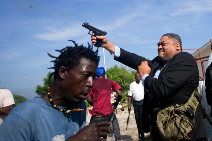 Ruling party Senator Ralph Fethiere fires his gun outside Parliament as he arrives for a ceremony to ratify Fritz William Michel's nomination as prime minister in Port-au-Prince, Haiti, Monday, Sept. 23, 2019. Opposition members confronted ruling-party senators, and Fethiere pulled a pistol when protesters rushed at him and members of his entourage. (AP Photo/Dieu Nalio Chery) thegrio.com