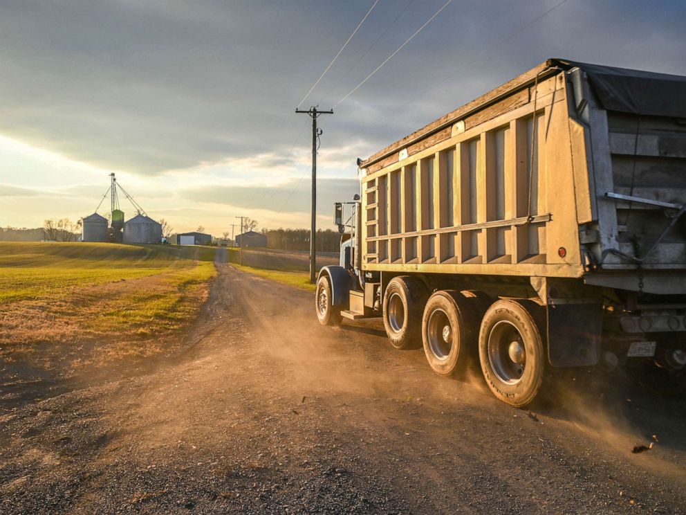 PHOTO: A roll off truck drives down dirt road towards grain silos, Laytonsville Maryland.