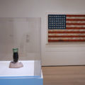 Marisol’s 1962 'Love' sculpture made from plaster and a Coca-Cola bottle sits in front of Jasper Johns’s 'Flag', 1954–55.