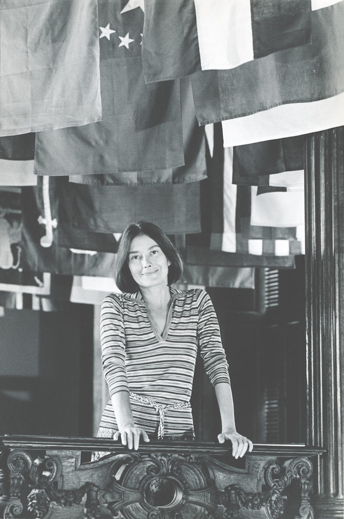 Lisa Taylor on the grand stair of the Carnegie Mansion in 1976, with a display of flags from the inaugural exhibition "MAN transFORMs."