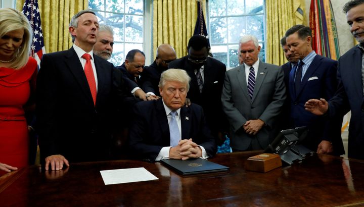 Faith leaders place their hands on the shoulders of President Donald Trump as he takes part in a prayer for those affected by