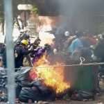 Protesters run past burning debris as