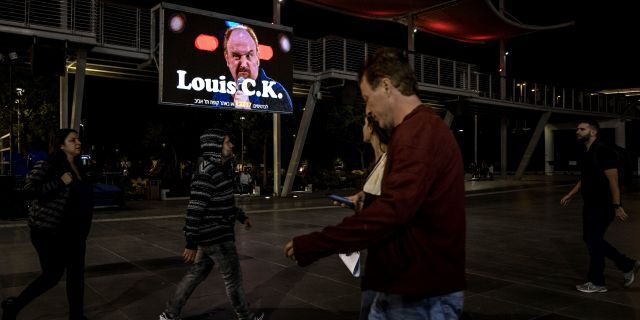 In this Thursday, Nov. 28, 2019 photo, Israelis walk past a billboard showing Comedian Louis C.K. in the Israeli city of Holon near Tel Aviv. Two years after being swept up in the Me Too movement and acknowledging sexual misconduct with multiple women, comedian Louis C.K. took to the stage at a nearly packed basketball arena outside Tel Aviv, where the audience seemed ready to let it go.(AP Photo/Tsafrir Abayov)