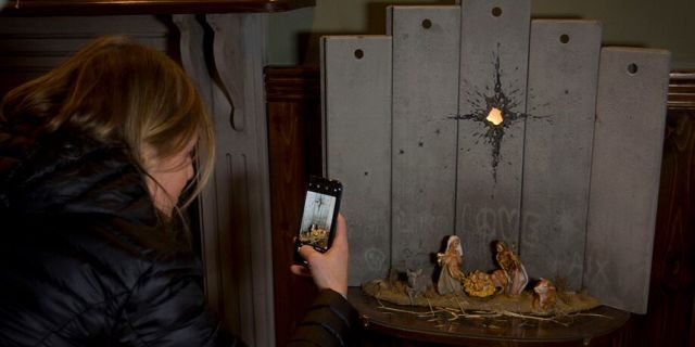 A Christian visitor takes pictures of a new artwork dubbed "Scar of Bethlehem" by the artist Banksy displayed in The Walled Off Hotel, in the West Bank city of Bethlehem, Sunday, Dec. 22, 2019. (AP Photo/Majdi Mohammed)