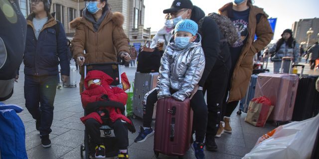 Travelers wear face masks as they walk outside of the Beijing Railway Station in Beijing.