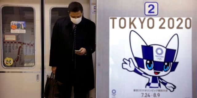 A poster promoting the Tokyo 2020 Olympics is posted next a train door as a commuter wearing a mask looks at his phone in a train, Friday, Jan. 31, 2020, in Tokyo. 