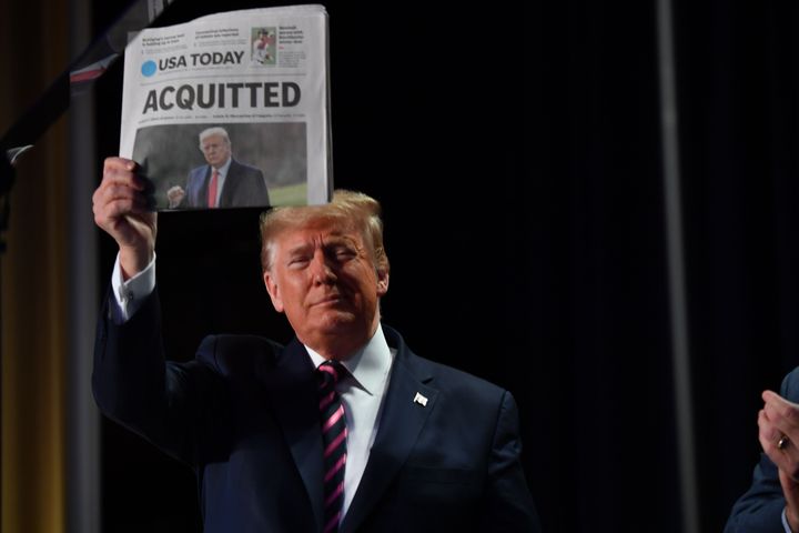 US President Donald Trump holds up a newspaper that displays a headline "Acquitted" as he arrives to speak at the 68th annual
