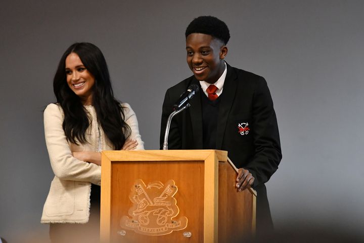 The Duchess of Sussex smiles as student Aker Okoye speaks during a school assembly.
