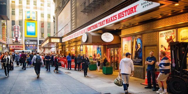 New York City Manhattan Broadway theater district street scene with many people walking besides the famous theaters.