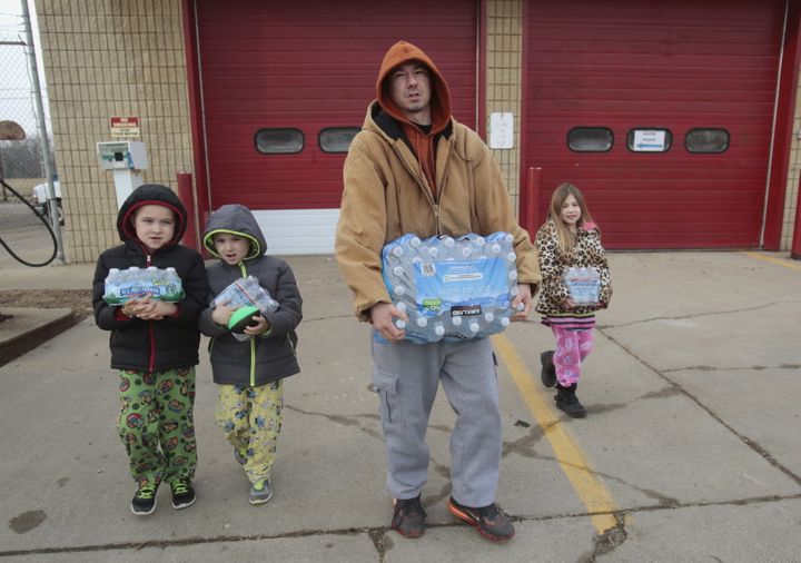 Flint resident Jerry Adkisson and his children carry water bottles from a fire station.&nbsp;