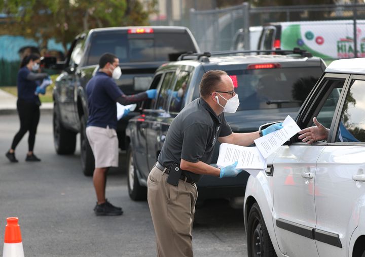 Eddie Rodriguez (right) and other Hialeah city employees hand out unemployment applications to people in their vehicles in fr