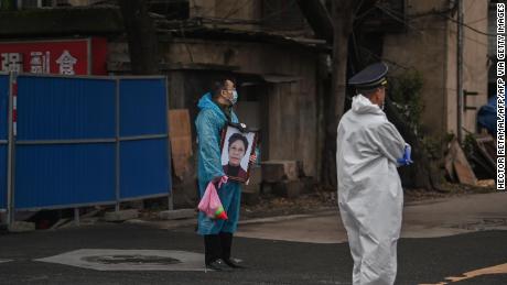 A man wearing a mask and a blue raincoat holds a portrait as he stands outside the Biandanshan cemetery in Wuhan on March 31.