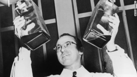 Jonas Salk holds up two decanters containing the anti-polio vaccine that he developed. 