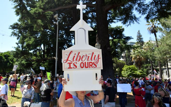 A woman help up a sign depicting a church as hundreds of people gathered earlier this month to protest the stay-at-home order