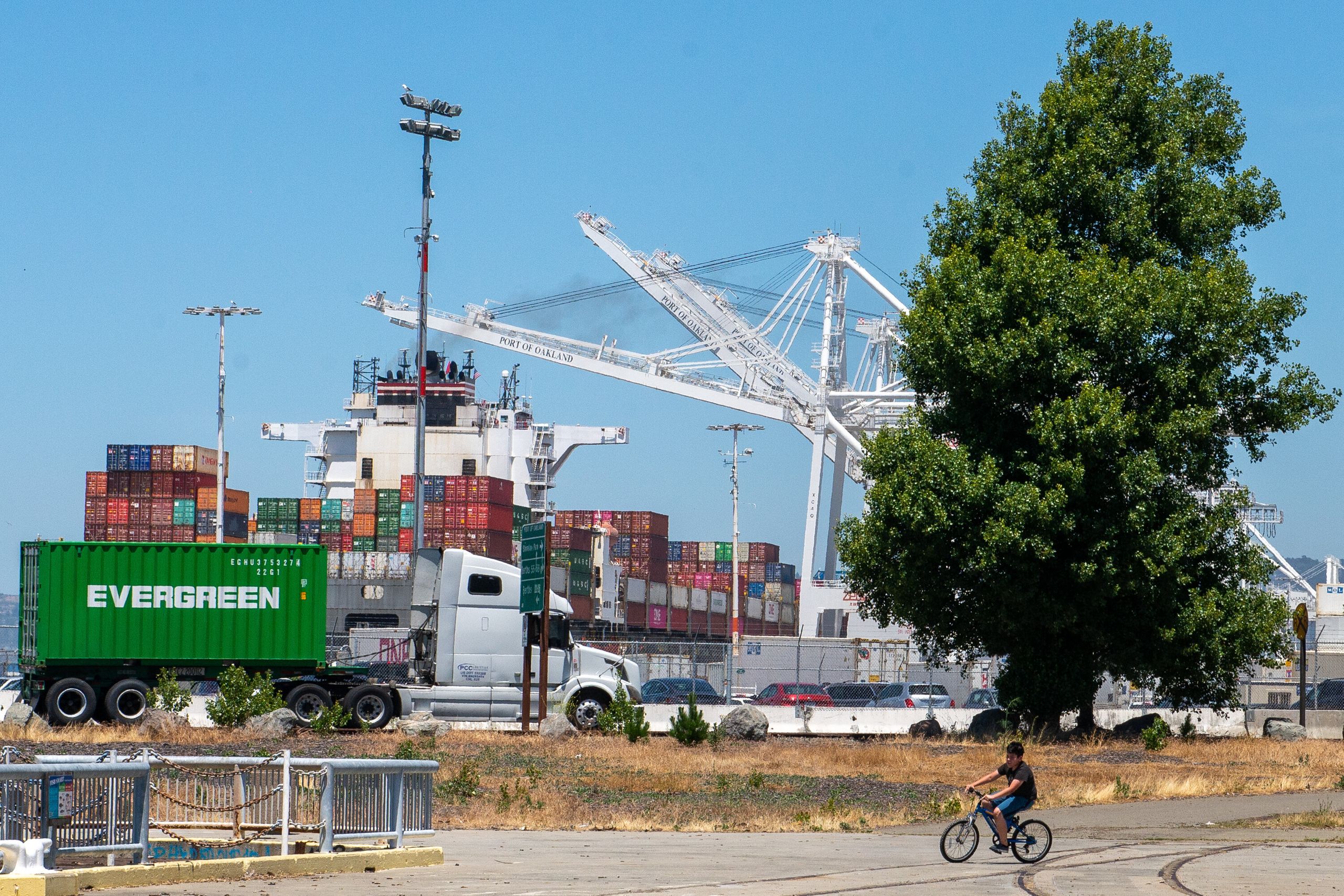 Ken Vasquez, 10, rides his bike at Middle Harbor Shoreline Park while shipping trucks haul freight at the Port of Oakland. Ne