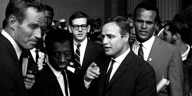 American actor Charleton Heston (1923 - 2008) (left) and singer Harry Belafonte (right, with a button on his lapel), writer James Baldwin (1924 - 1987) (center left) talks with actor Marlon Brando (1924 - 2004) in the Lincoln Memorial during the March on Washington for Jobs and Freedom, Washington DC, August 28, 1963. The march and rally provided the setting for the Reverend Martin Luther King Jr's iconic 'I Have a Dream' speech.