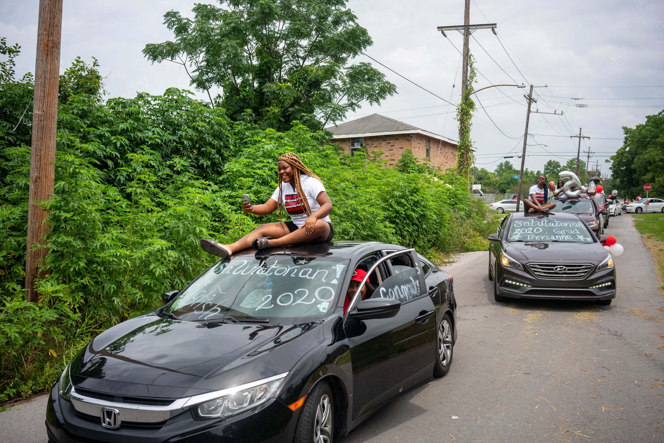 Trevianne Turner rides on top of her sister's car during a Dr. Martin Luther King Jr. High School graduation parade through t