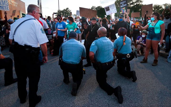Police officers from Ferguson, Missouri, join protesters to remember George Floyd by taking a knee in the parking lot of the 