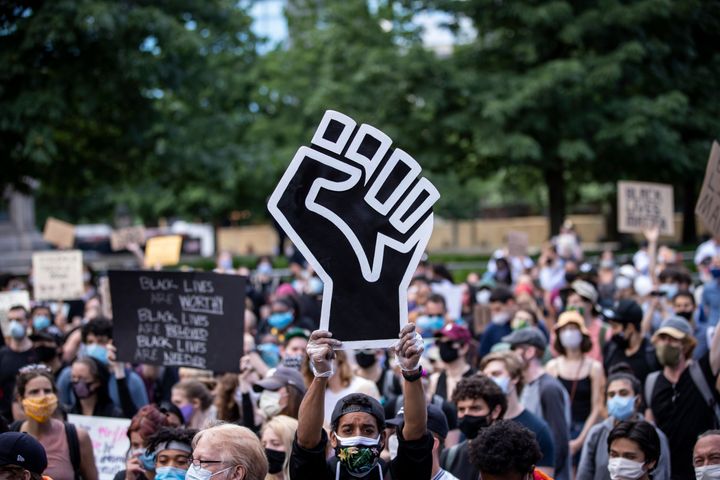 A protester wearing a mask holds a large Black power raised fist in the middle of a crowd that gathered at Columbus Circle on