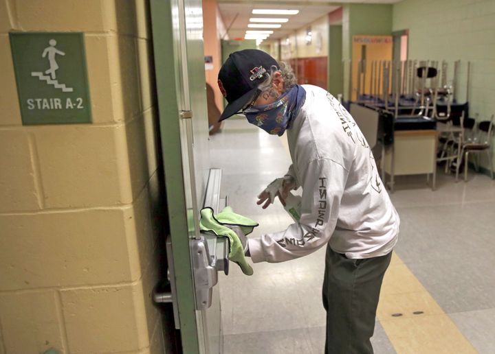 A custodian wipes down a hallway doorway at the Mildred Avenue K-8 School building in Boston ahead of the school reopening la